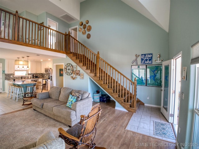 living area featuring light tile patterned flooring, plenty of natural light, a high ceiling, and stairs