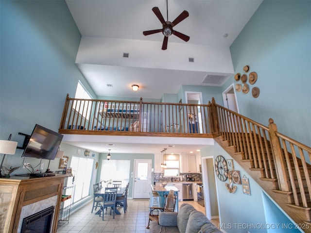 living area with visible vents, stairway, a high ceiling, a ceiling fan, and a glass covered fireplace