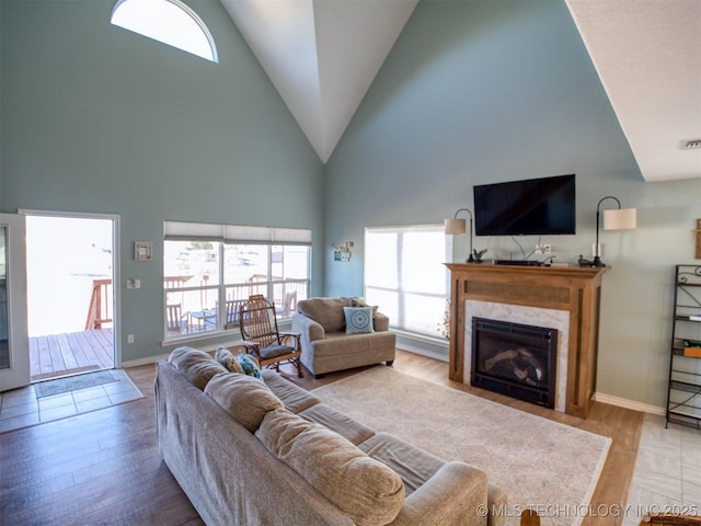 living room with light wood-type flooring, baseboards, a premium fireplace, and high vaulted ceiling