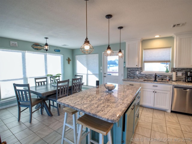 kitchen with visible vents, dishwasher, a center island, white cabinetry, and a sink