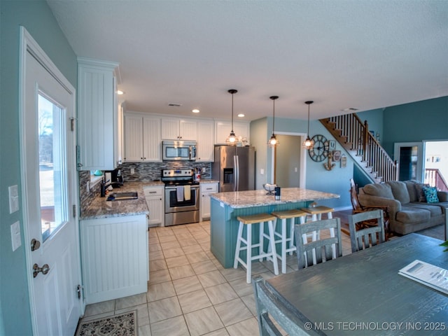 kitchen with hanging light fixtures, a kitchen island, white cabinetry, and stainless steel appliances