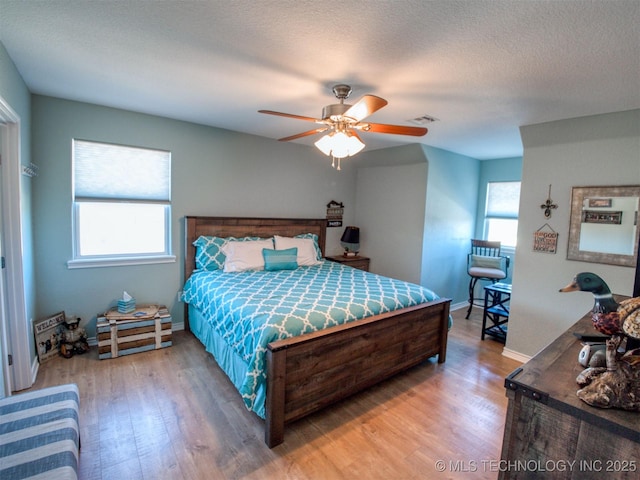 bedroom featuring light wood-type flooring, visible vents, a textured ceiling, and multiple windows