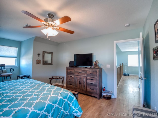 bedroom featuring light wood finished floors, ceiling fan, multiple windows, and baseboards