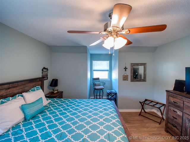 bedroom with a ceiling fan, a textured ceiling, baseboards, and wood finished floors