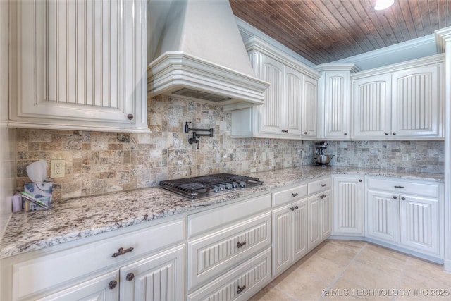 kitchen featuring white cabinets, custom range hood, light stone countertops, tasteful backsplash, and stainless steel gas stovetop