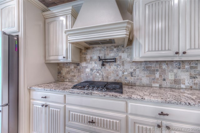 kitchen featuring stainless steel appliances, white cabinetry, custom exhaust hood, decorative backsplash, and light stone countertops