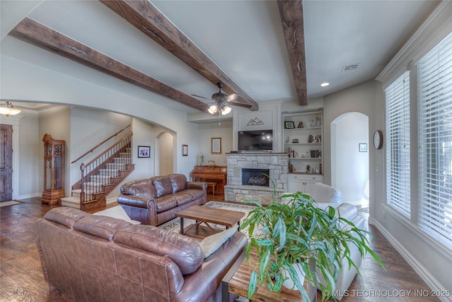 living room with wood finished floors, visible vents, baseboards, a stone fireplace, and arched walkways
