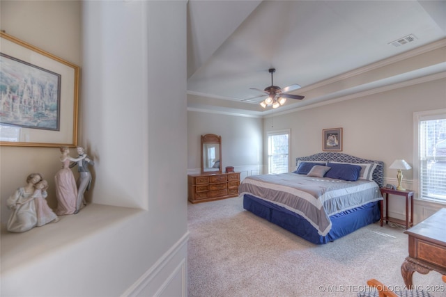 bedroom with a tray ceiling, visible vents, crown molding, and light carpet