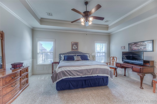 bedroom featuring light carpet, a wainscoted wall, a tray ceiling, and ornamental molding