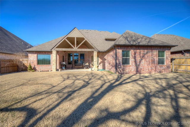 rear view of house featuring brick siding, roof with shingles, a patio area, and fence private yard