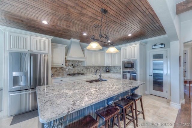 kitchen with stainless steel appliances, a sink, white cabinets, an island with sink, and custom range hood