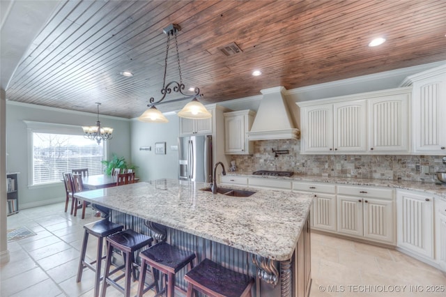 kitchen featuring appliances with stainless steel finishes, a sink, an island with sink, and custom exhaust hood