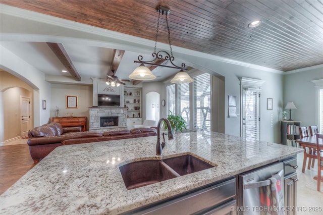 kitchen featuring a ceiling fan, dishwasher, a sink, arched walkways, and a fireplace