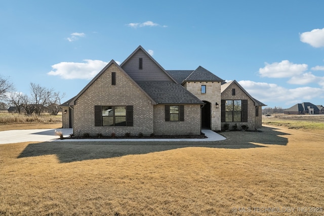 view of front of property featuring a shingled roof, brick siding, and a front lawn