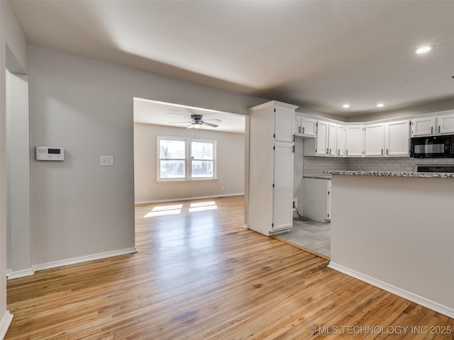 kitchen featuring light wood finished floors, white cabinetry, black microwave, and decorative backsplash