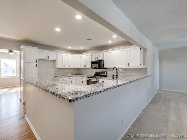 kitchen with a peninsula, stainless steel range with gas cooktop, black microwave, and light stone counters