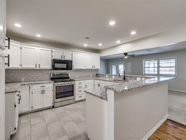 kitchen with black microwave, a peninsula, a sink, white cabinets, and gas stove