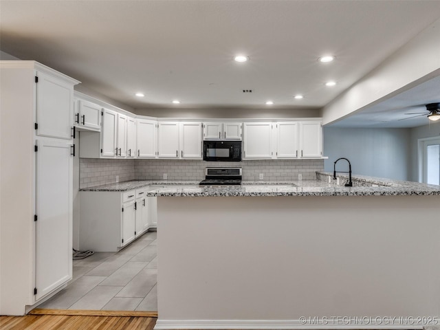 kitchen with light stone counters, stove, white cabinetry, black microwave, and a peninsula