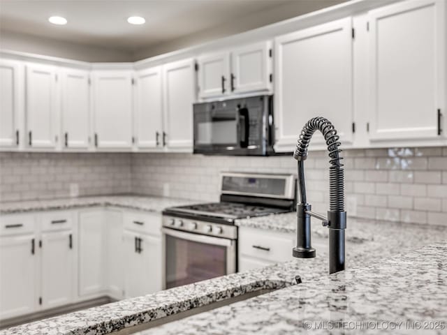 kitchen with black microwave, stainless steel gas range oven, decorative backsplash, light stone counters, and white cabinetry