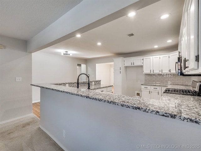 kitchen with white cabinets, stove, a peninsula, and light stone countertops