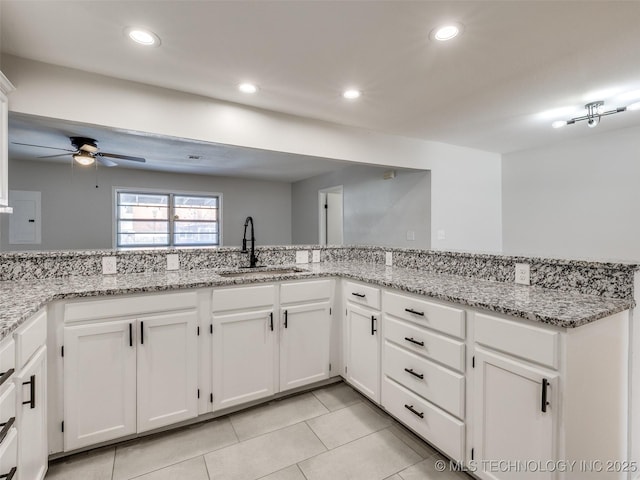 kitchen featuring light stone countertops, white cabinetry, a sink, and recessed lighting