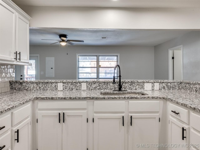 kitchen featuring light stone counters, white cabinets, a sink, and ceiling fan