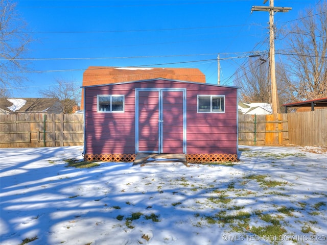 snow covered structure with a fenced backyard, an outdoor structure, and a shed