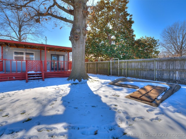 yard covered in snow featuring fence and a wooden deck