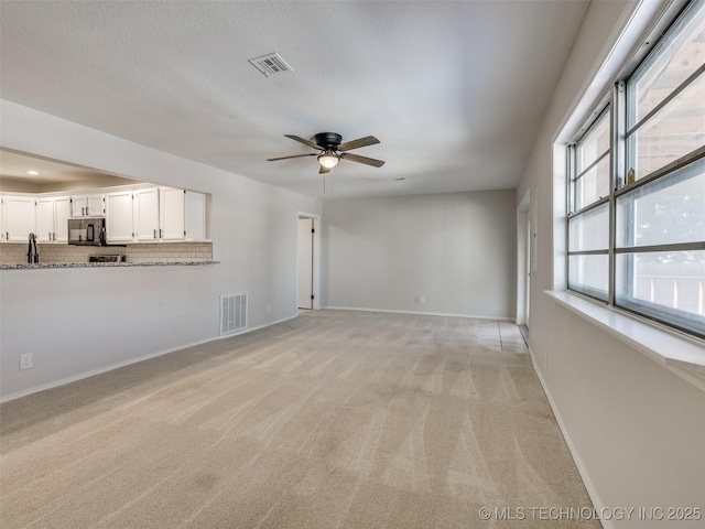 unfurnished living room with ceiling fan, light colored carpet, visible vents, and baseboards