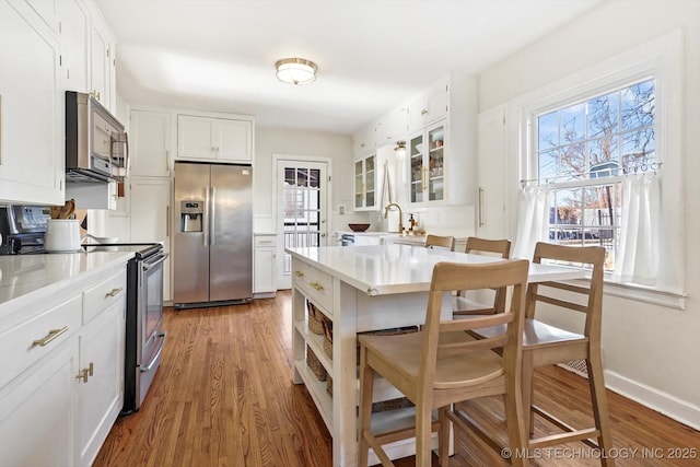 kitchen featuring white cabinetry, light countertops, appliances with stainless steel finishes, a wealth of natural light, and glass insert cabinets