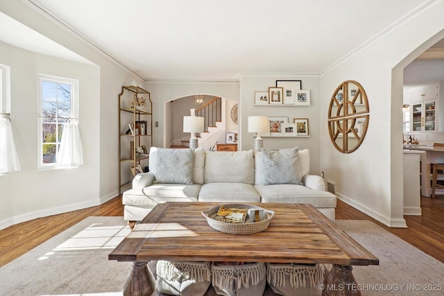 living area featuring light wood-style flooring, stairs, arched walkways, and ornamental molding