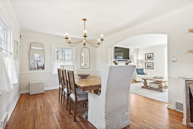 dining area featuring arched walkways, crown molding, radiator heating unit, and wood finished floors