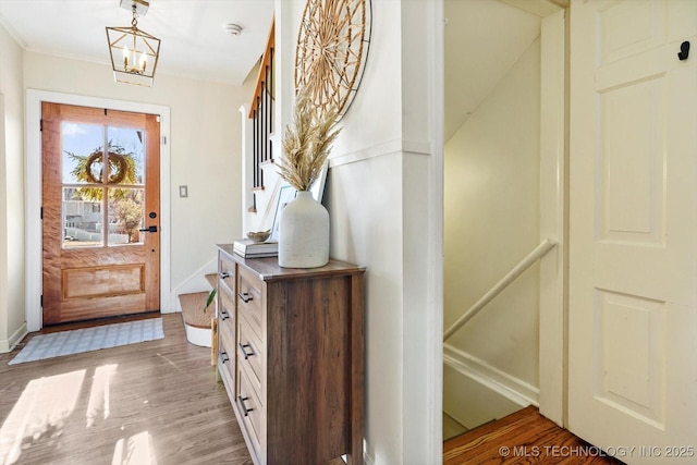 entryway featuring baseboards, a chandelier, wood finished floors, and ornamental molding