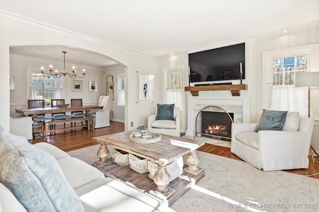 living room featuring ornamental molding, arched walkways, a fireplace, and wood finished floors