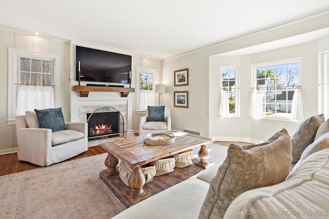 living room featuring wood finished floors, visible vents, baseboards, a lit fireplace, and crown molding