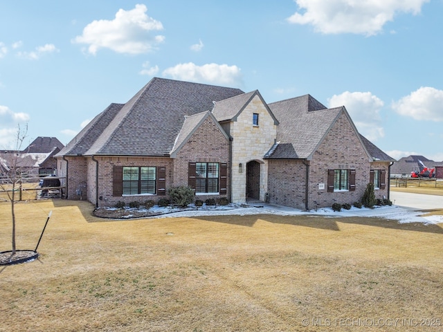 french country inspired facade with a front yard, stone siding, brick siding, and fence