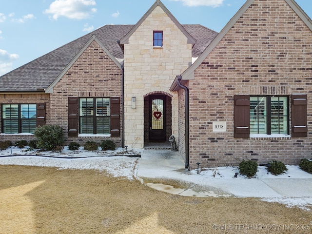 french provincial home with stone siding, roof with shingles, a lawn, and brick siding