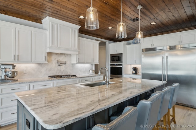 kitchen with built in appliances, a large island, a sink, and white cabinets