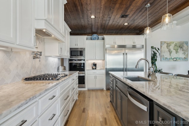 kitchen with appliances with stainless steel finishes, light stone counters, white cabinetry, pendant lighting, and a sink