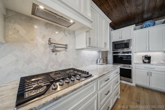 kitchen featuring stainless steel appliances, white cabinets, backsplash, and light stone countertops