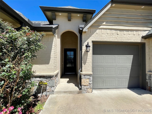 view of exterior entry featuring a garage, concrete driveway, and brick siding