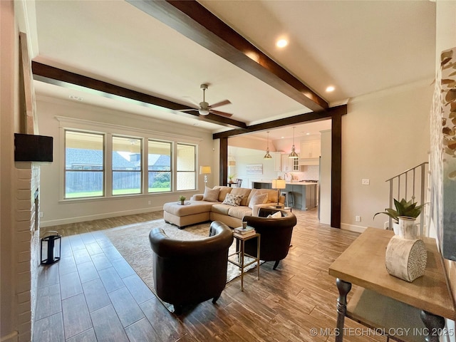 living area featuring ceiling fan, baseboards, beam ceiling, and wood finished floors