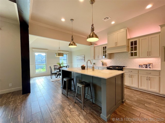 kitchen with dark wood-style flooring, tasteful backsplash, visible vents, glass insert cabinets, and an island with sink