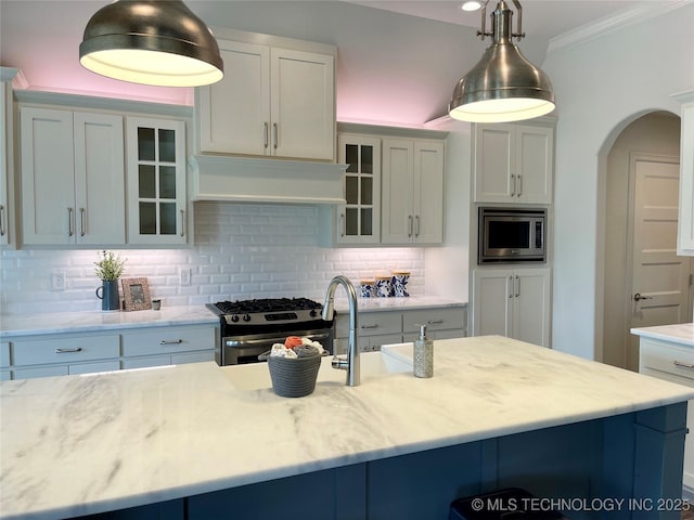 kitchen featuring under cabinet range hood, appliances with stainless steel finishes, glass insert cabinets, and backsplash