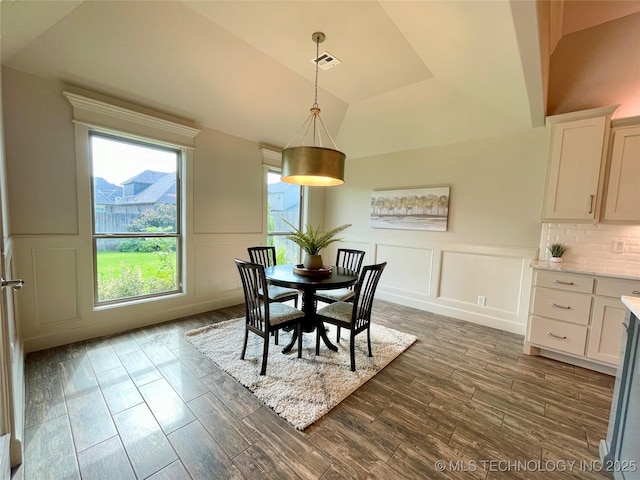 dining room featuring vaulted ceiling, dark wood finished floors, visible vents, and a decorative wall