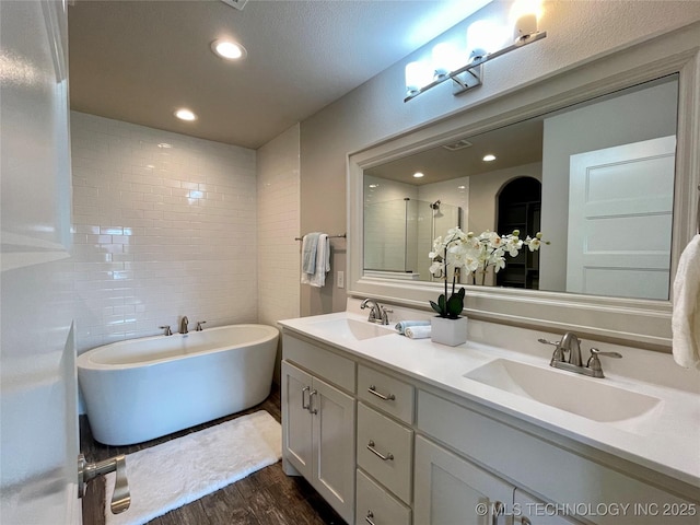 full bathroom featuring double vanity, wood finished floors, a soaking tub, and a sink