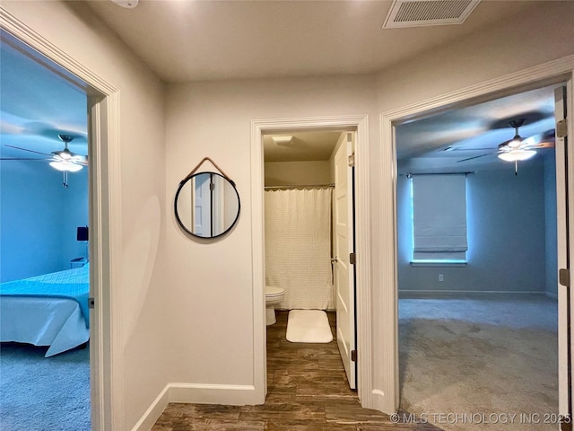 hallway with dark wood-style floors, baseboards, visible vents, and dark carpet