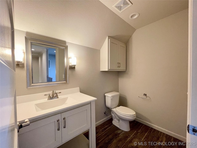 bathroom featuring toilet, wood finished floors, vanity, visible vents, and vaulted ceiling