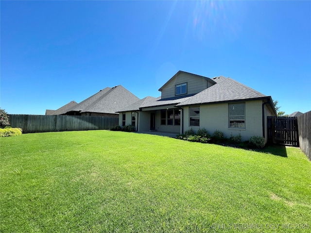 back of property with a fenced backyard, a shingled roof, a lawn, and brick siding