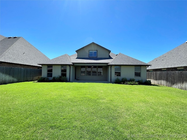 back of house with a shingled roof, a lawn, and a fenced backyard